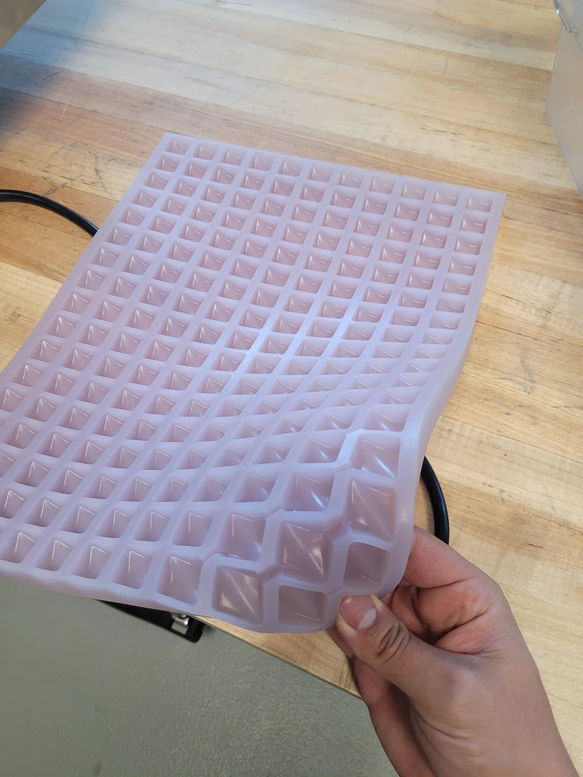 A silicone mold flexed by hand, showing square cavities.